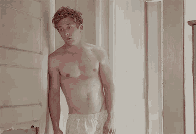 a shirtless man leaning against a wall with a triangle tattoo on his chest