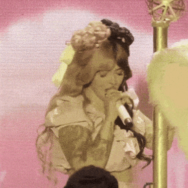 a woman singing into a microphone in front of a pink backdrop