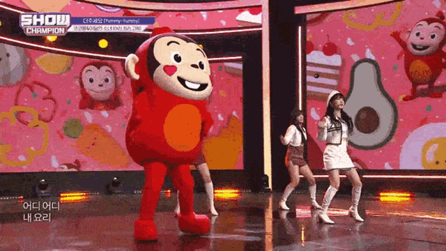 a group of girls are dancing on a stage with a monkey mascot in the background