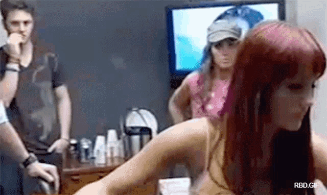 a woman with red hair is standing in front of a television while a man stands behind her