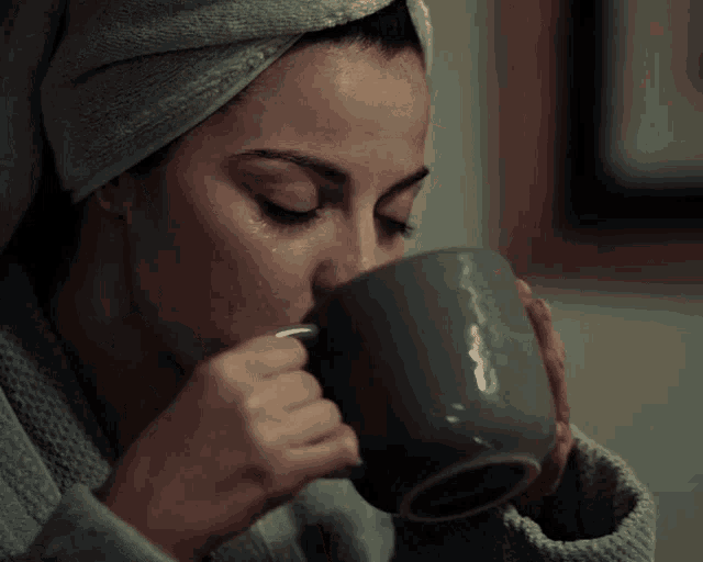 a woman with a towel wrapped around her head is drinking from a cup