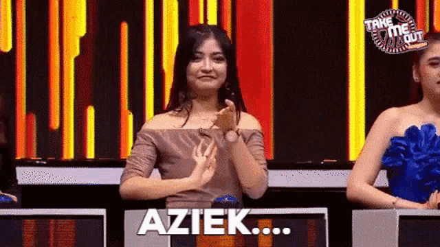 a woman applauds in front of a sign that says " aziek "