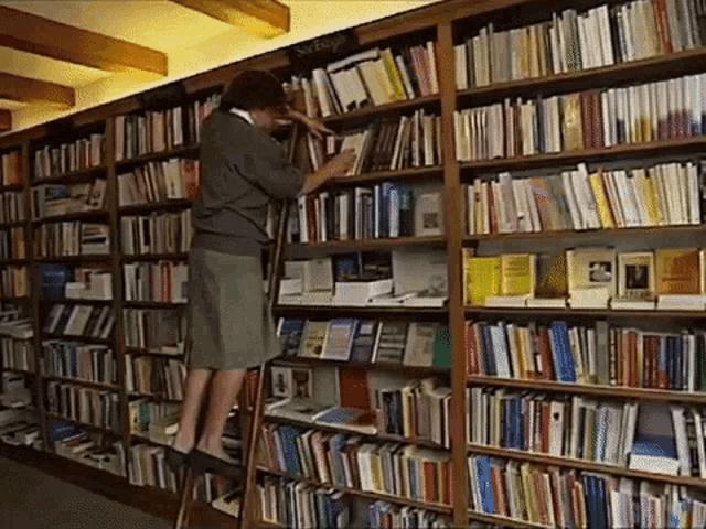 a woman is standing on a ladder in a book store looking at books