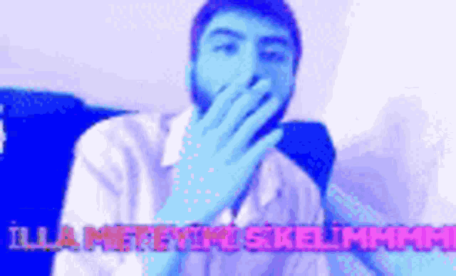 a man with a beard is covering his mouth with his hand while sitting on a blue couch .