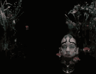 a woman with a snake on her head is surrounded by flowers .