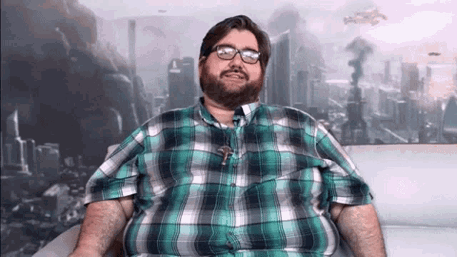 a man wearing glasses and a plaid shirt is sitting on a couch with a city in the background