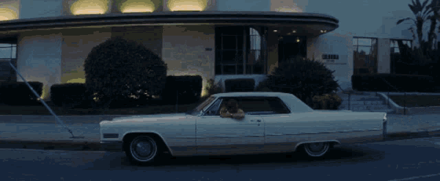a white car is driving down a street in front of a building that has a no parking sign