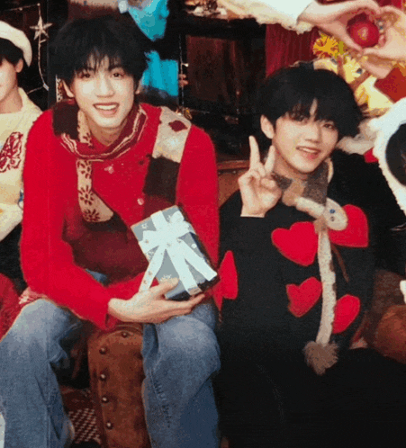 a boy in a red sweater is holding a gift box and giving the peace sign