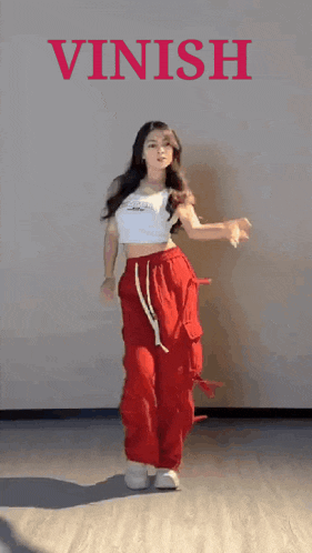 a woman in a white top and red pants is dancing in front of a wall that says vinish