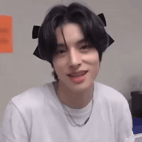 a young man with a bow in his hair is wearing a white shirt and necklace .