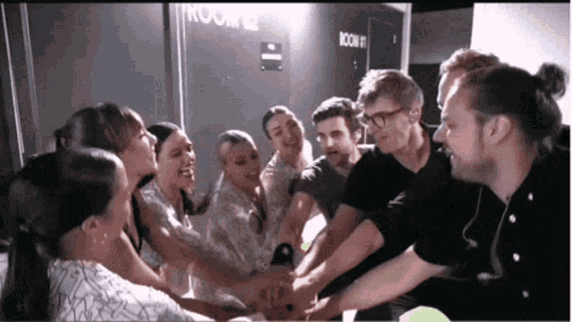 a group of people are putting their hands together in front of a room that says room 2