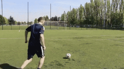 a man in a blue shirt is kicking a soccer ball on a field