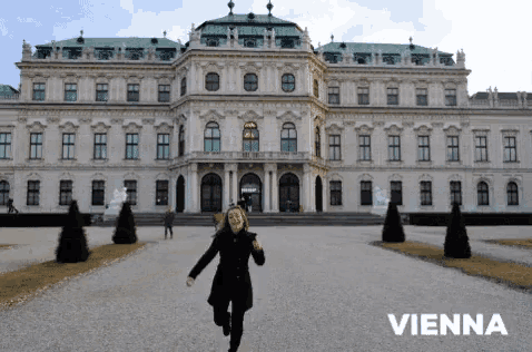 a woman is running in front of a large white building with vienna written on it