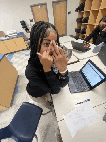 a girl sitting at a desk making a funny face
