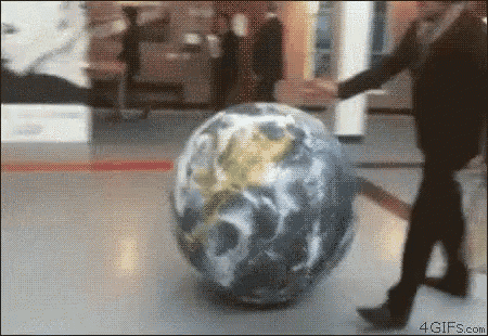 a man is pushing a large inflatable globe in a hallway
