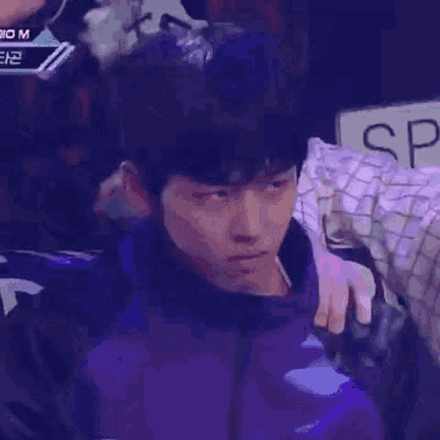 a young man in a purple jacket is sitting in a chair with a person holding his head .