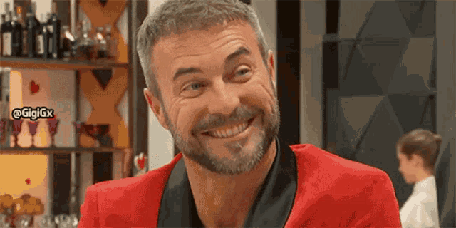 a man with a beard wearing a red jacket is smiling in front of a bar