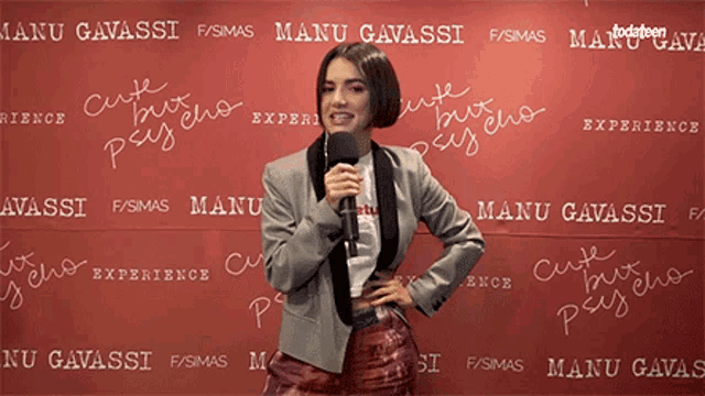 a woman is standing in front of a wall that says manu gavassi