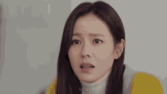 a close up of a woman 's face with a yellow sweater and a white turtleneck .