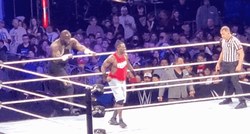 a man in a red tank top with nike on it is in a wrestling ring with a referee