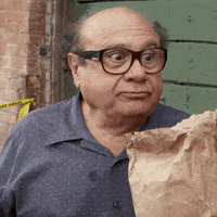 a bald man wearing glasses holds a brown paper bag