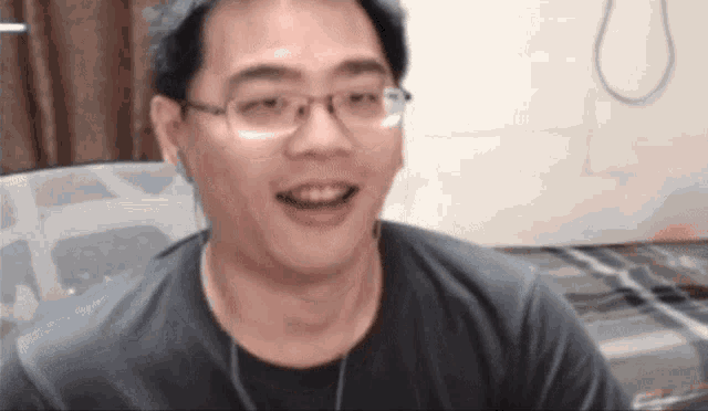 a man wearing glasses and ear buds is smiling while sitting on a bed .