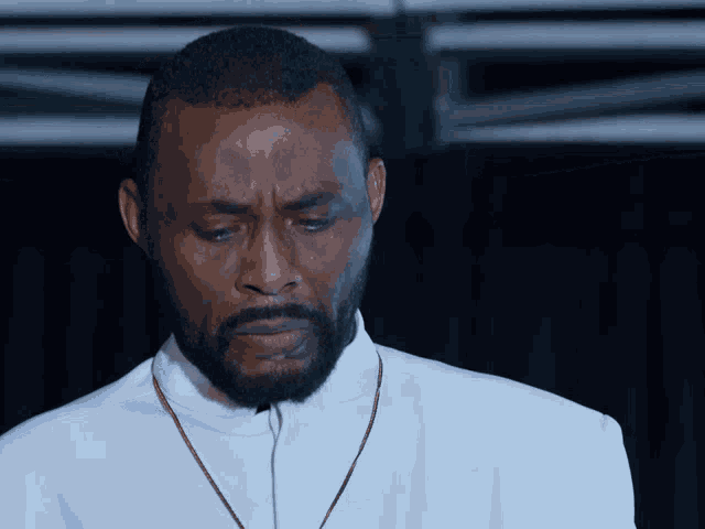 a man with a beard is wearing a white shirt and a brown necklace