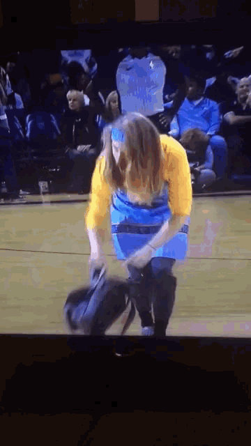 a woman in a yellow shirt and blue apron is kneeling on a basketball court