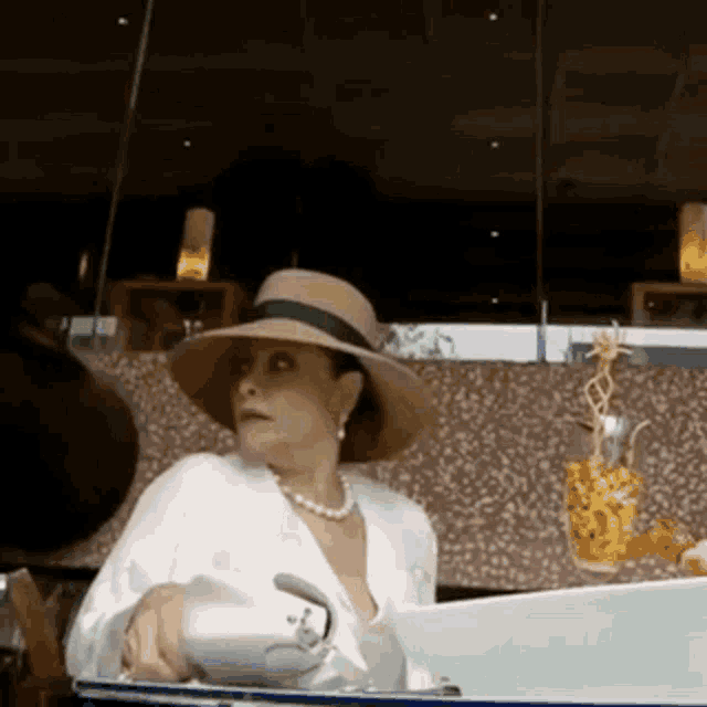 a woman wearing a hat and a pearl necklace is sitting in front of a laptop .
