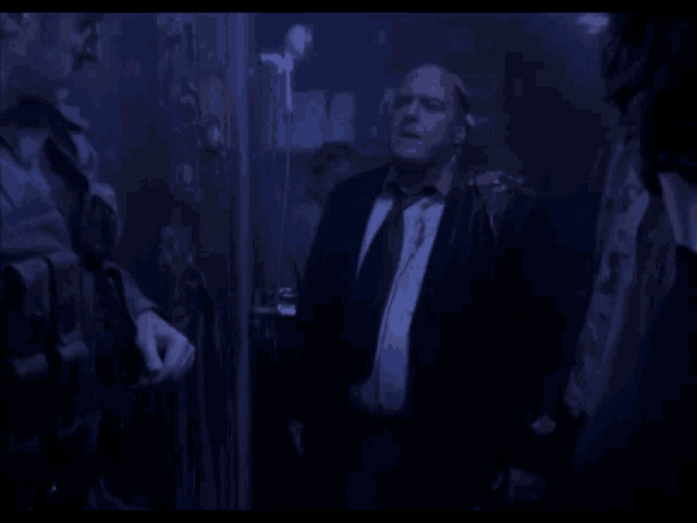 a man in a suit and tie is standing in a dark room with other people