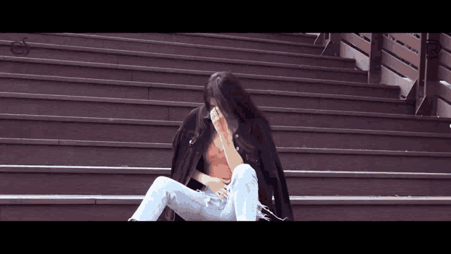 a woman is sitting on a set of stairs covering her face