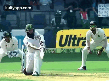 a group of cricket players are playing a game on a field with an ultra cement ad in the background .