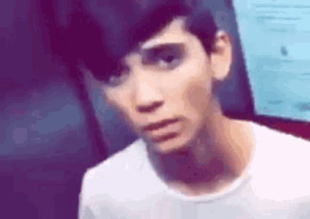 a young man in a white shirt is making a funny face while looking at the camera .