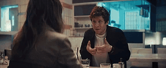 a man is sitting at a table with a woman and talking to her .