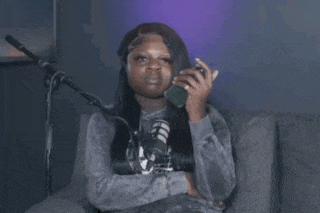 a woman is sitting in front of a microphone holding a cell phone