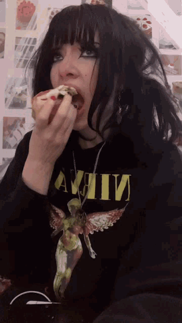 a girl wearing a black shirt that says nirvana is eating a cupcake