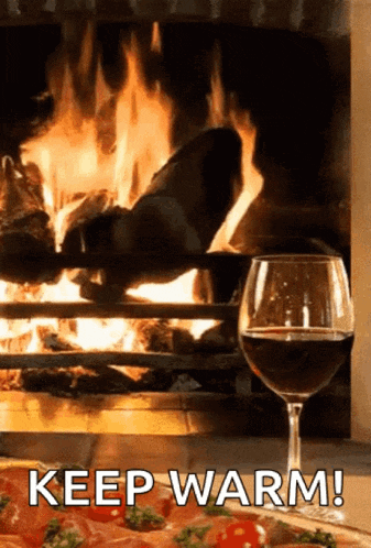 a glass of wine is sitting in front of a fireplace with the words keep warm written below it
