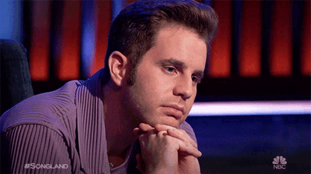a man sitting in a chair with his hands on his chin and the words songland on the bottom right