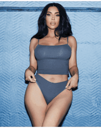 a woman in a crop top and high waisted briefs stands in front of a blue wall