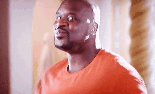 a man in an orange shirt is standing in a room looking up .