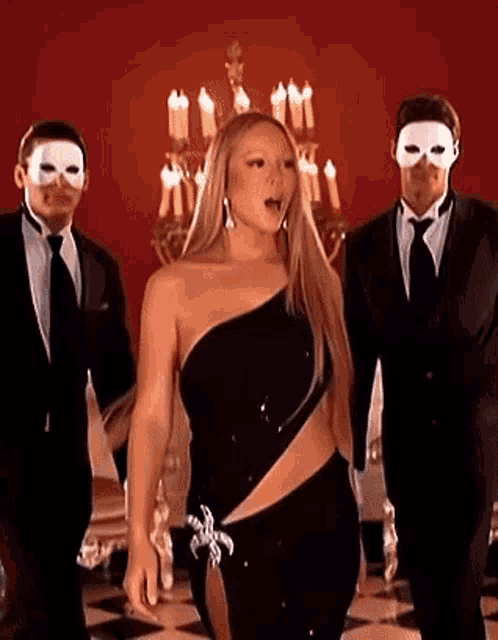 a woman in a black dress is standing in a room with two men in masks .