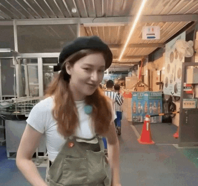 a woman wearing overalls and a black beret stands in a hallway