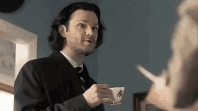 a man in a suit and tie is holding a cup of coffee and talking to a snail .