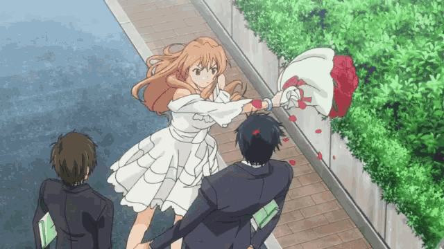 a woman in a white dress is throwing a bouquet of roses at a man .
