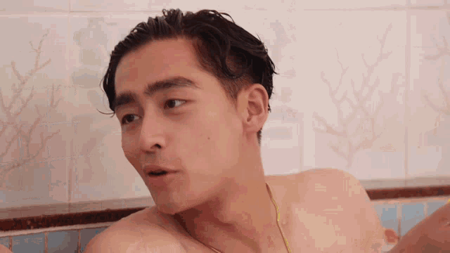 a shirtless man is sitting in a bathtub with a tiled wall behind him