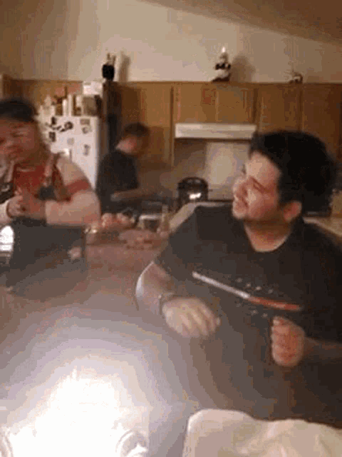 a man is sitting at a table in a kitchen holding a gun .