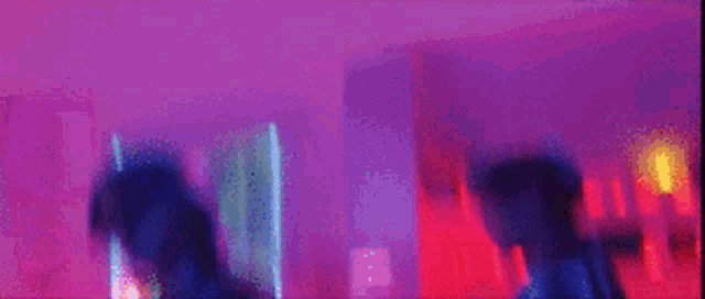 a blurry picture of two people standing next to each other in a room with purple and blue lights .
