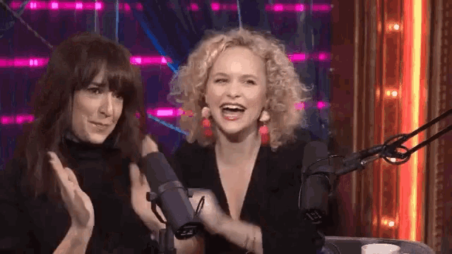 two women are sitting in front of a microphone and clapping .