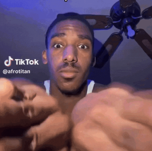 a man is making a funny face in front of a ceiling fan with tiktok written on it