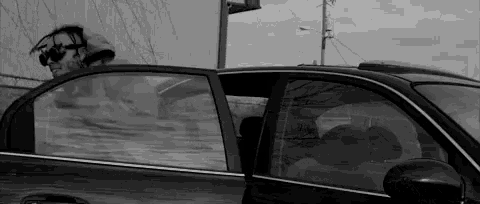 a black and white photo of a man in a car with his head out the window .